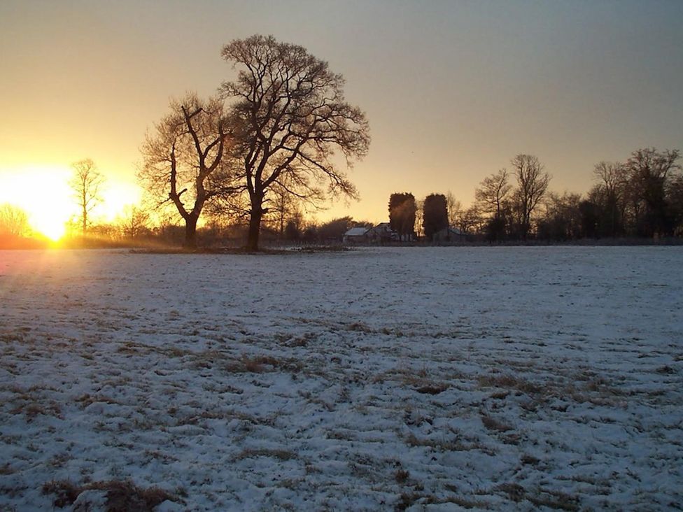 A snowy field with trees and a sunset at No 1 The Martins Walberswick