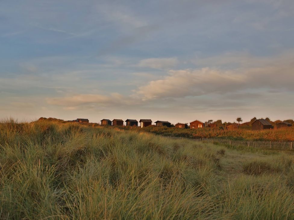Beach huts on sand dunes under clouds at No 1 The Martins Walberswick