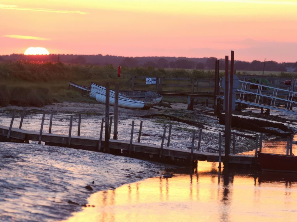 A sunset over water with a boat and jetty at No 1 The Martins Walberswick