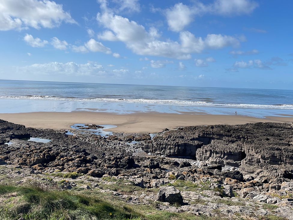 A beach with rocks and ocean under a blue sky at 7 Adrian Close Porthcawl