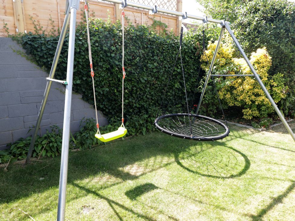 A swing set with a traditional swing and a nest swing in the garden at Ty Traeth in Porthcawl