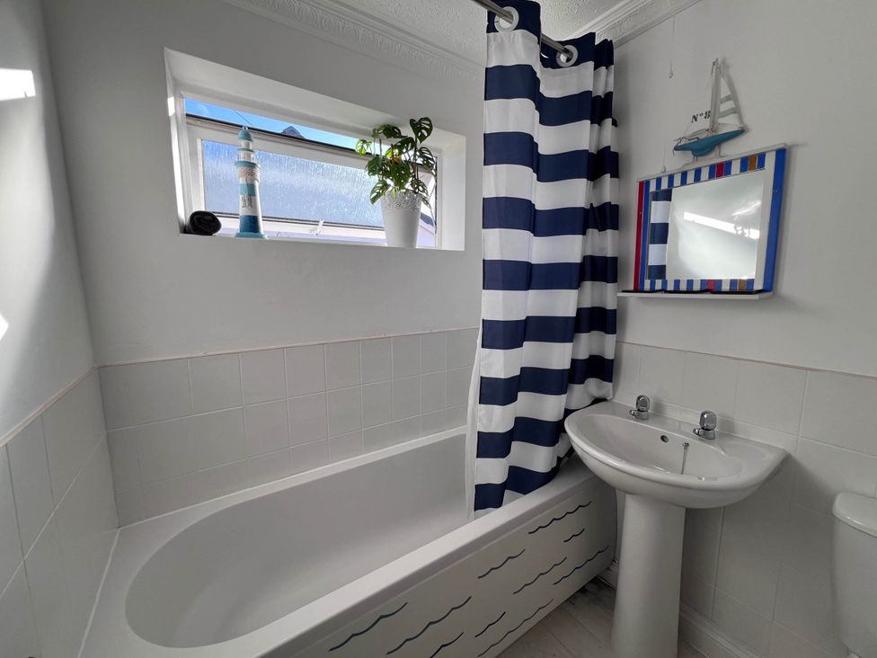 A bathroom with a bathtub, sink, and shower curtain at 2 Bed Family Bungalow, WiFi, Parking, Garden, Dogs in Pentraeth