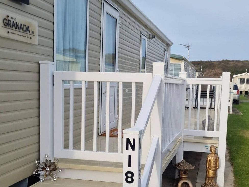 An outdoor view of a mobile home with a deck and steps at The Granada XL in a holiday park