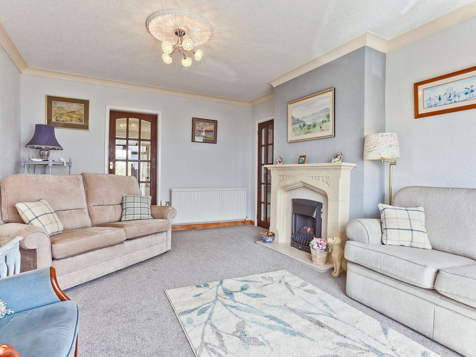 A living room with a sofa, armchair, fireplace, and wall art at Lothlorien in Grange over Sands