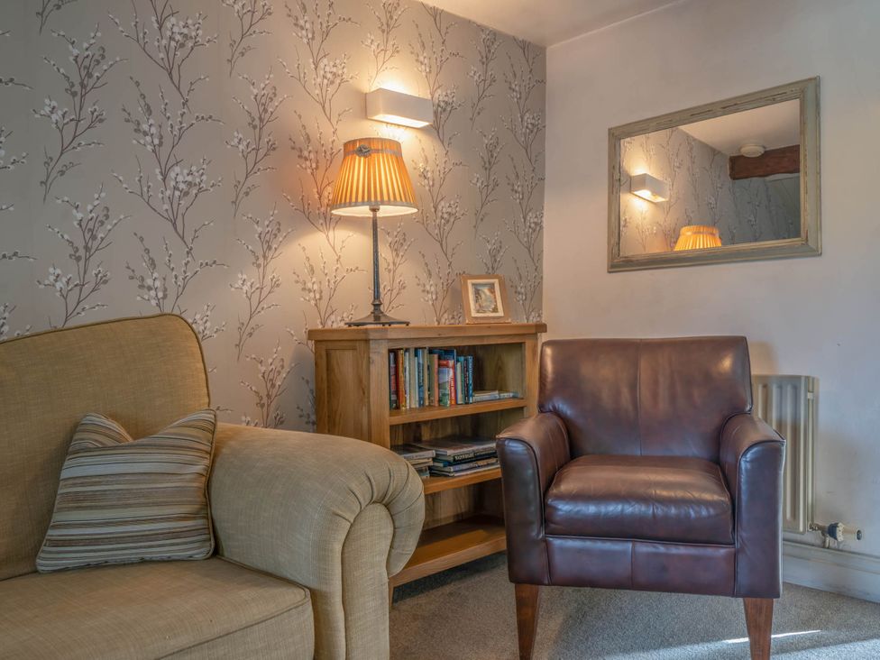 A living room with a sofa, armchair, and bookshelf at Cosy cottage near scenic walks and country pub, Penrith