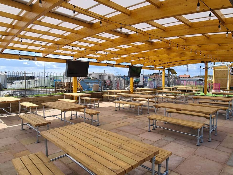 An outdoor seating area with wooden tables at Cayton Bay Lodge Parkdean Resorts Scarborough
