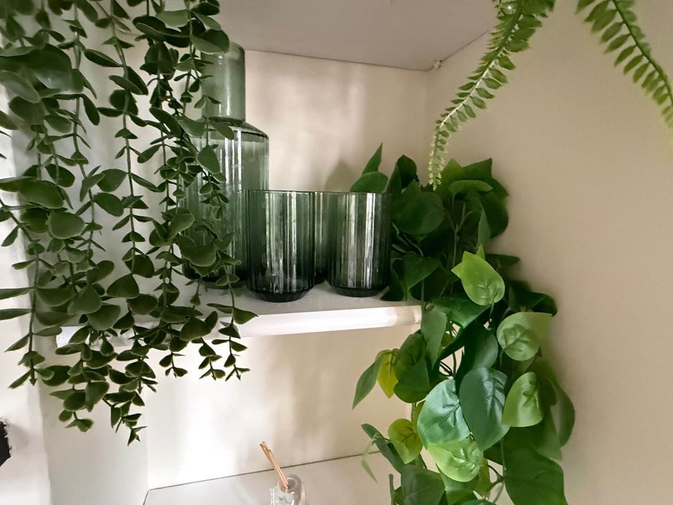 A shelf with green glass vases and drinking glasses along with artificial plants at Cotswolds Castle Sleeps 8 with Enclosed Garden in Banbury