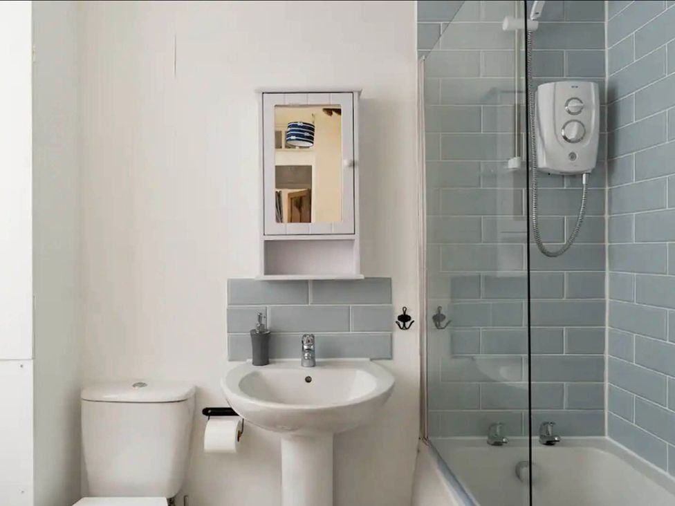 A bathroom with a toilet, sink, mirror, and shower at Beautiful Sea Front Cottage in the Ocean City, Plymouth