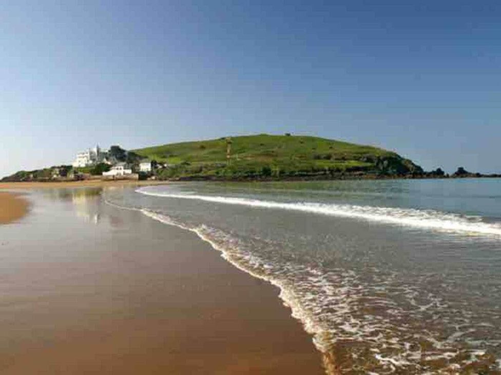 A beach with waves and a hill with buildings at 3Bed Cottage Plymouth Dog friendly Sleeps7, Plymouth