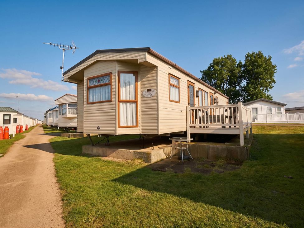 A static caravan with a deck and lawn area at a caravan park
