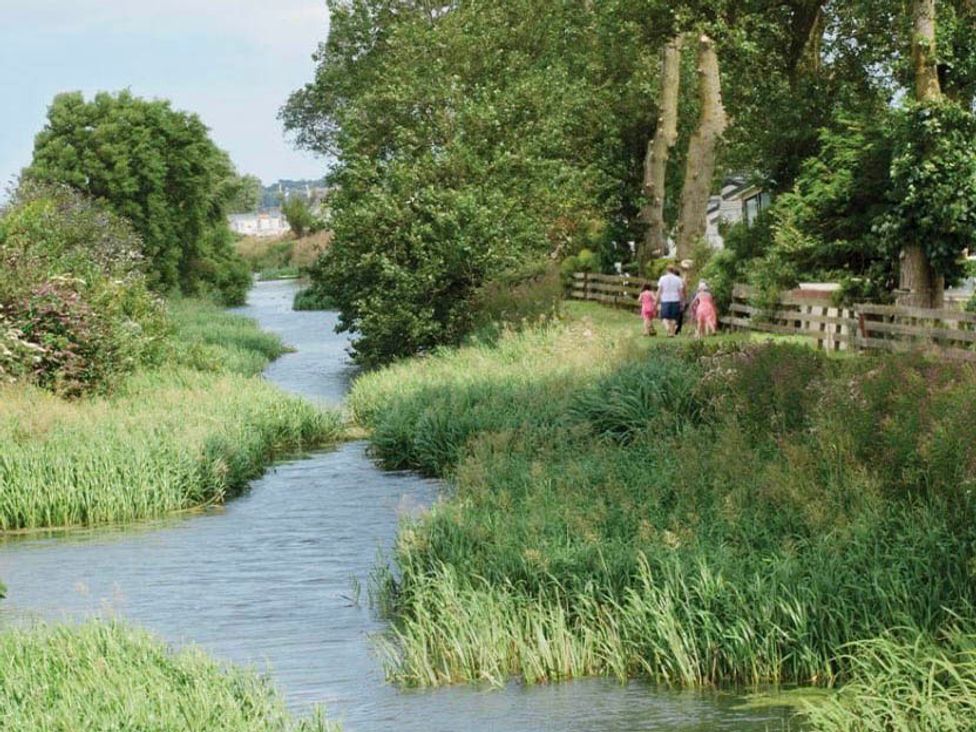 A river with grass and trees alongside a path at a scenic outdoor location