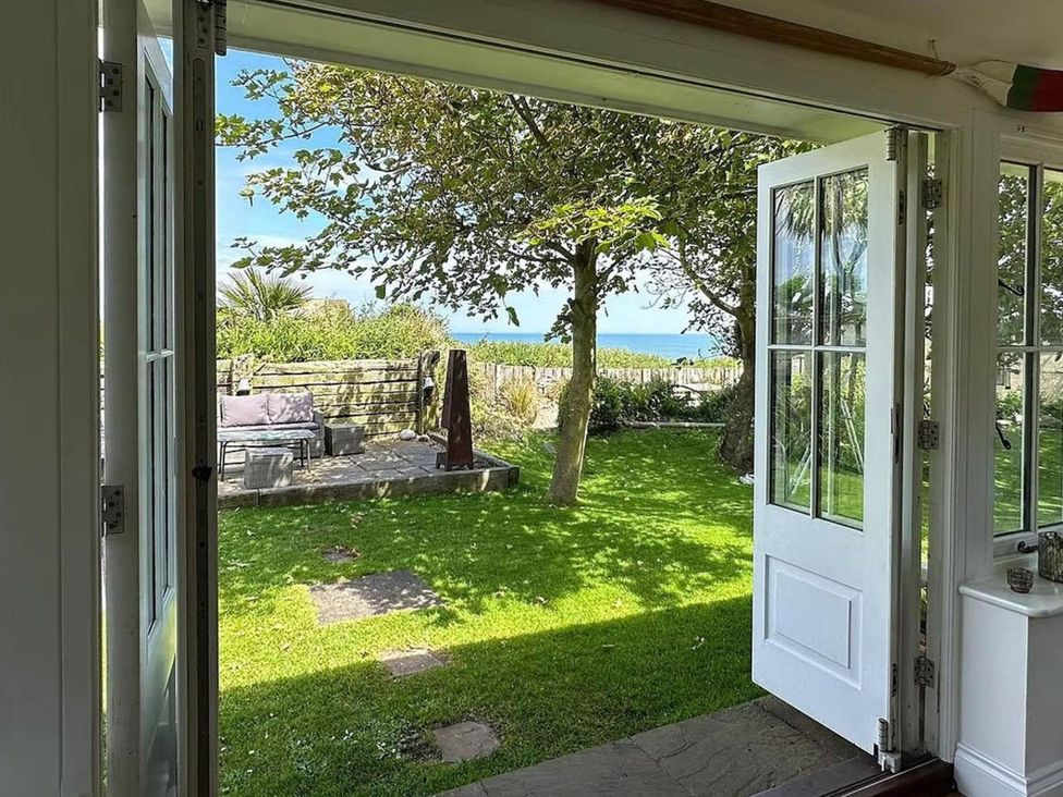 A view from an open door to a garden with furniture and trees at Norfolk Seaview Luxury Retreat with 7 Bedrooms in Mundesley