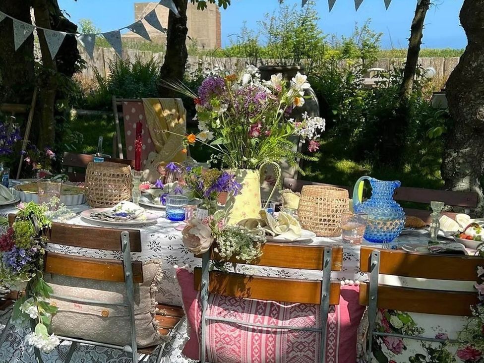 A garden table set with flowers and tableware at Norfolk Seaview Luxury Retreat with 7 Bedrooms in Mundesley