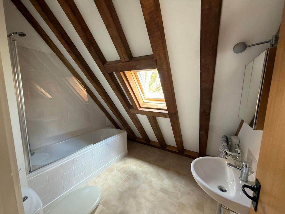 A bathroom with a bathtub, shower, sink and wood beams at Tremail near Camelford