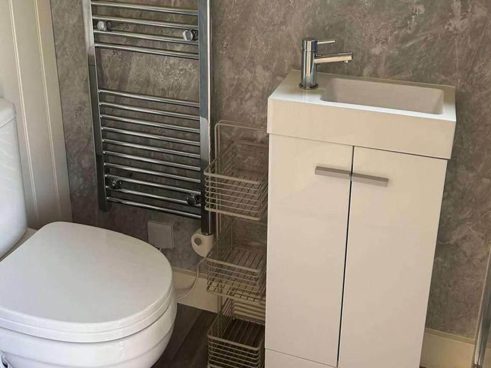 A bathroom with a toilet, sink, towel radiator, and storage basket near Bishop's Waltham