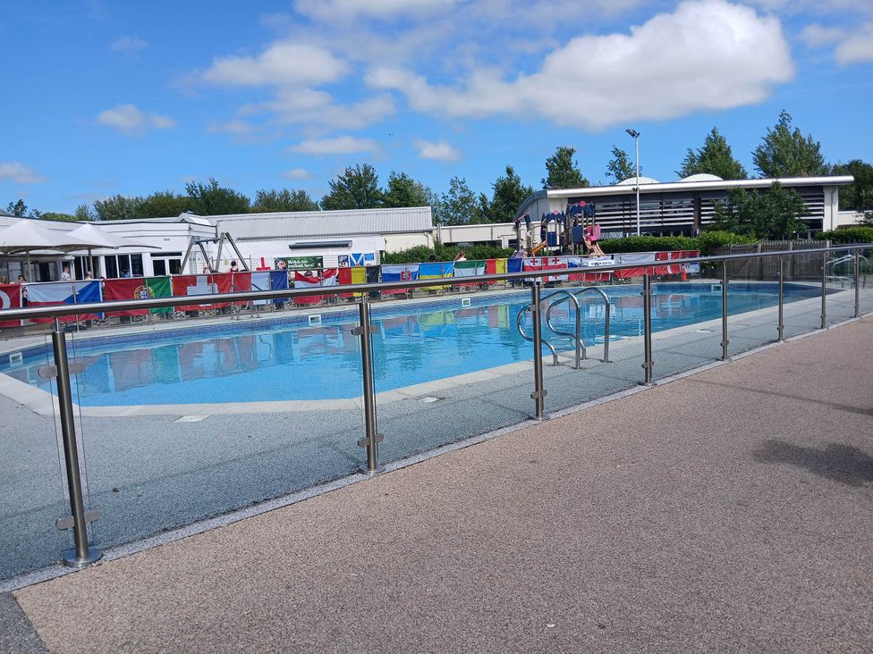 An outdoor swimming pool with flags and buildings at a recreational facility near Flookburgh