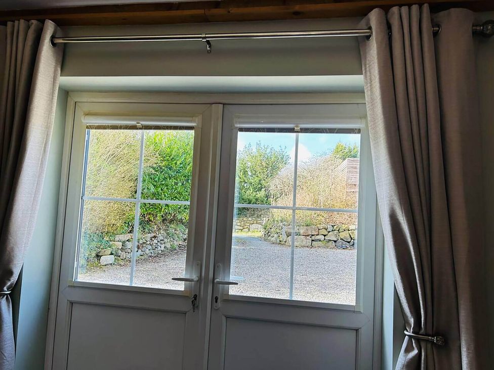 A window with curtains showing a gravel path and stone wall at 