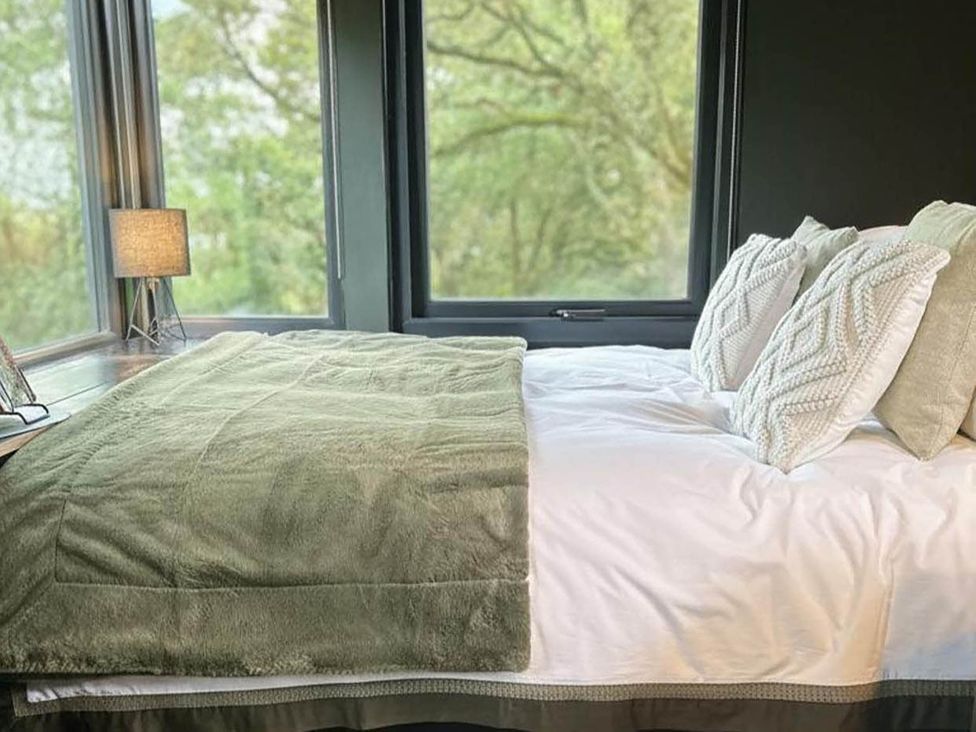 A bed with pillows and a blanket near a window at The Old Barn in Newton Abbot
