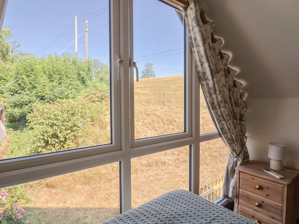 A bedroom view through a window with a bed and nightstand at The Linhay Cotleigh Nr. Honiton
