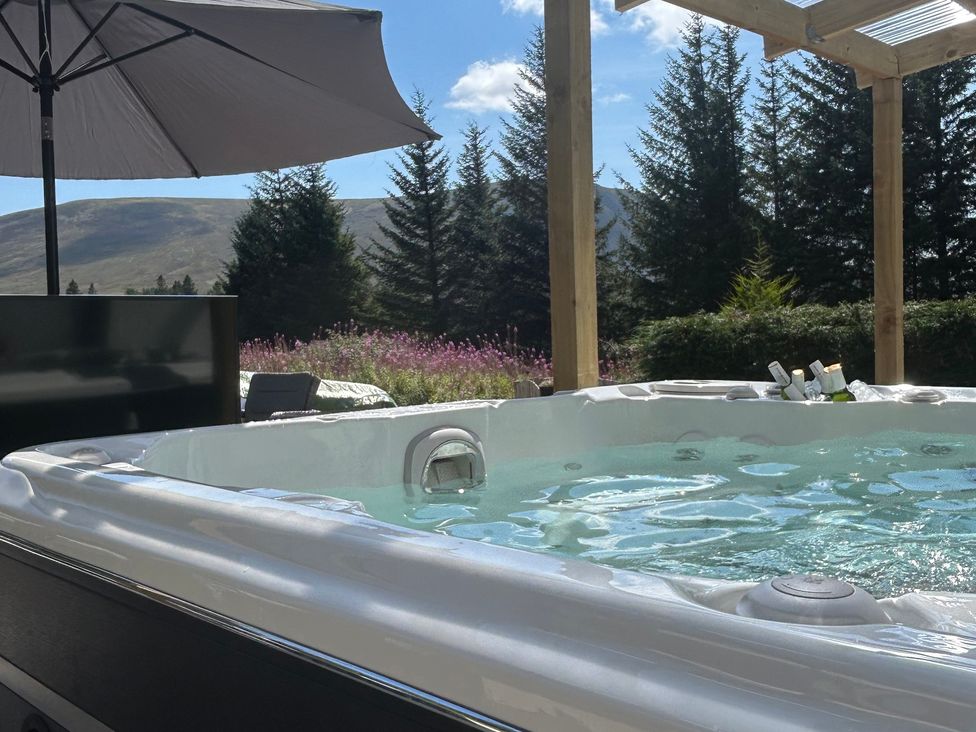 A hot tub with an umbrella and a television at 1 Station Cottages