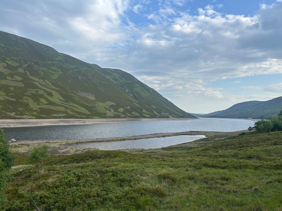 A lake surrounded by mountains with grass in the foreground at 1 Station Cottages