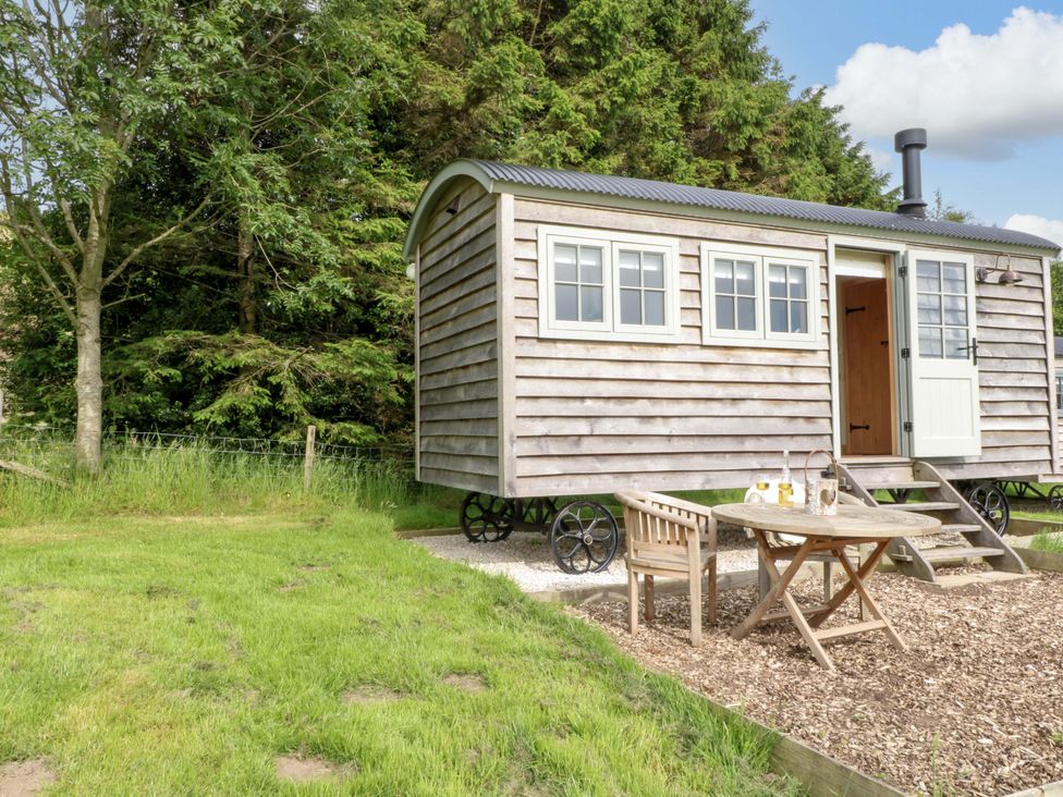 A shepherd's hut with a table and chairs outside at Pike House Farm Shepherds Hut 2 in Ashbourne