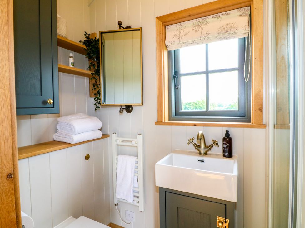A bathroom with a sink, mirror, and shelves at Pike House Farm Shepherds Hut 2 Thorpe near Ashbourne