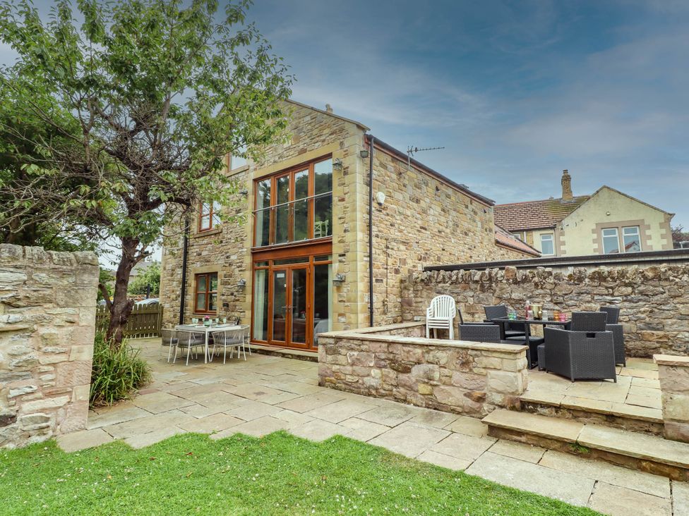 An outdoor patio with stone wall and furniture at Alma House in Seahouses