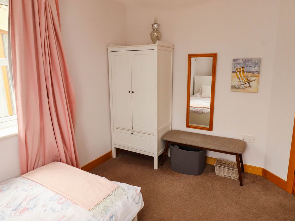 A bedroom with a bed, wardrobe, mirror, bench, and basket at Alma House in Seahouses