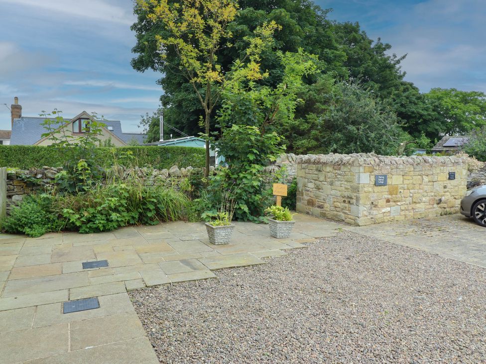 An outdoor area with a car parked and plants near a stone wall at Alma House in Seahouses