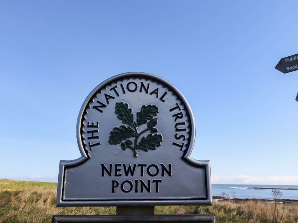 A sign for The National Trust at Newton Point with a coastline in the background