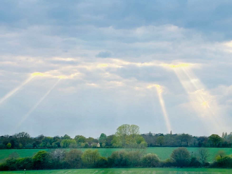 A view of rays of sunlight breaking through clouds over a green landscape at Fables Cottage in Otley, Suffolk