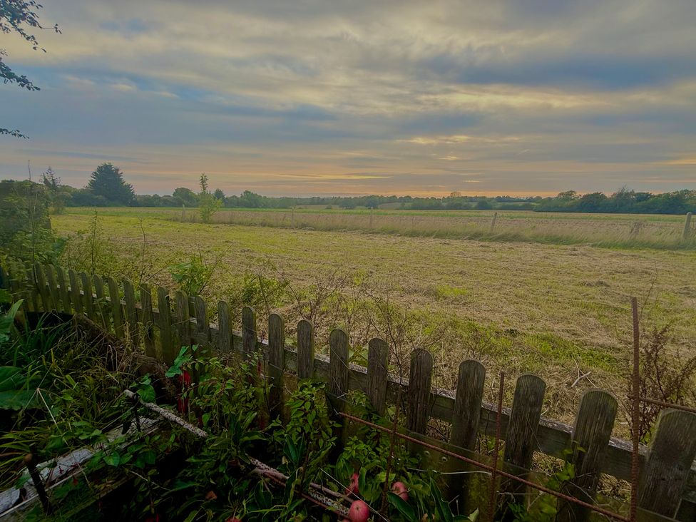 A view of a field with a fence and trees at Fables Cottage in Otley, Suffolk