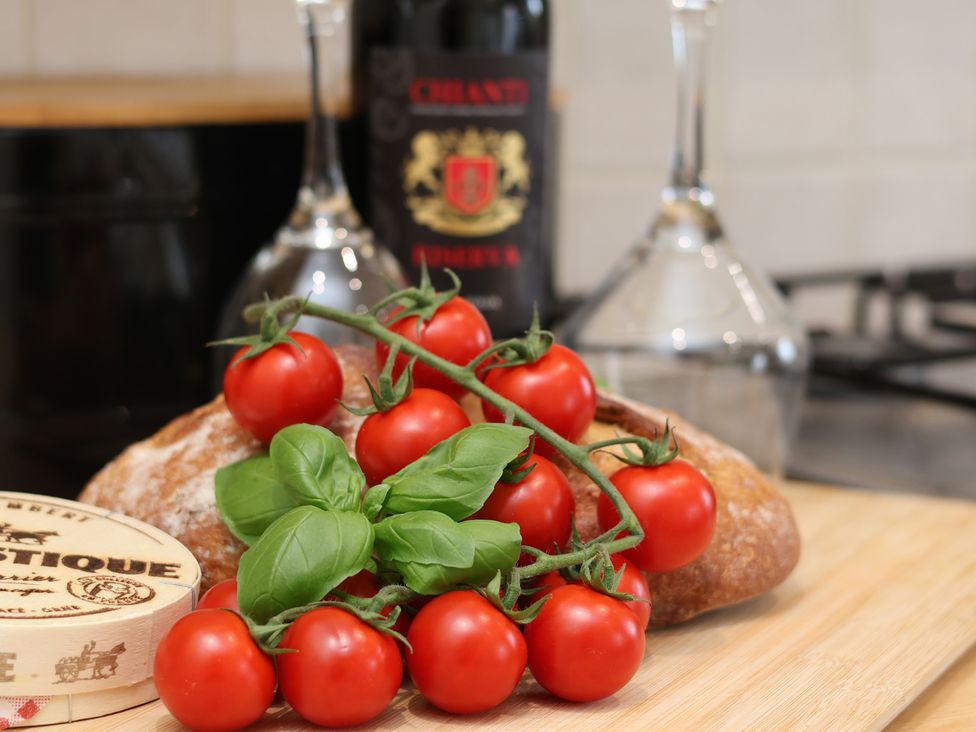 A kitchen counter with tomatoes, basil, bread, wine bottle, and wine glasses at The Cosy Haven in Malton