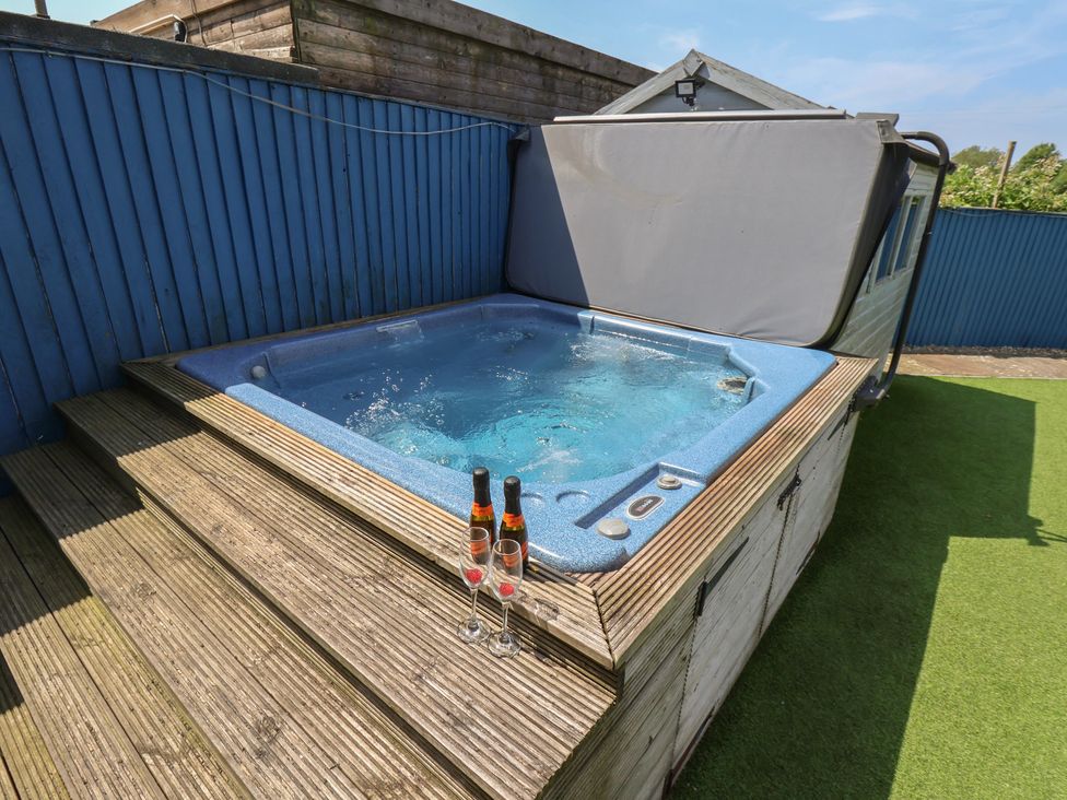 A hot tub on a wooden deck with glasses and bottles at The Cosy Haven in Malton
