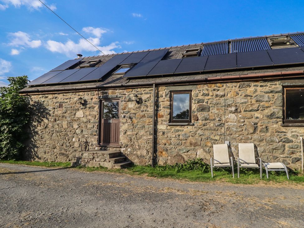 An outdoor view of a stone building with solar panels and chairs at Pandy Farmhouse