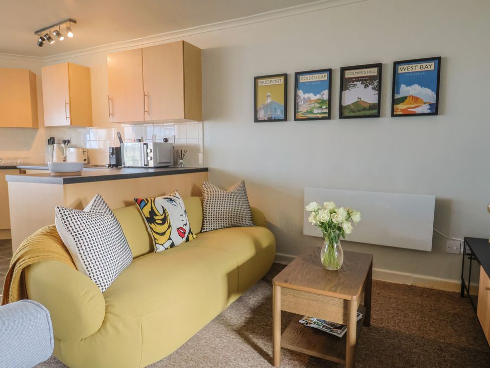 A living room with a yellow sofa and a vase of flowers at 4 Kingfisher Court West Bay