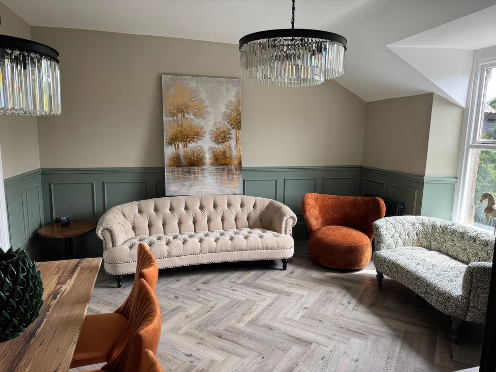 A living room with a sofa, armchair, side table, and chandelier at The Buxton Suite in Buxton