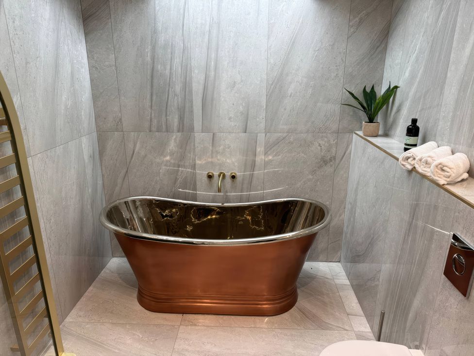 A bathroom with a copper bathtub and towels at The Buxton Suite in Buxton