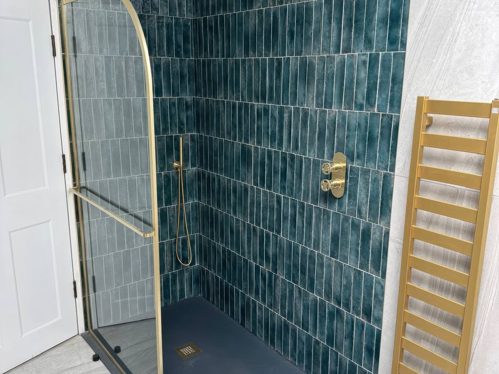 A shower area with green tiled walls and a gold shower door at The Buxton Suite in Buxton
