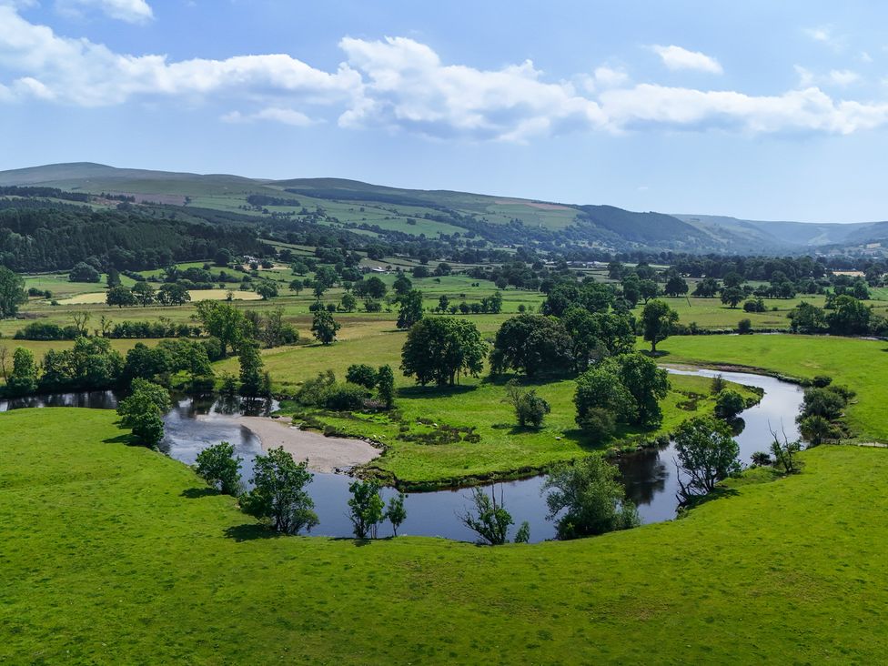 A scenic landscape with a river winding through fields and trees at The Granary in Corwen