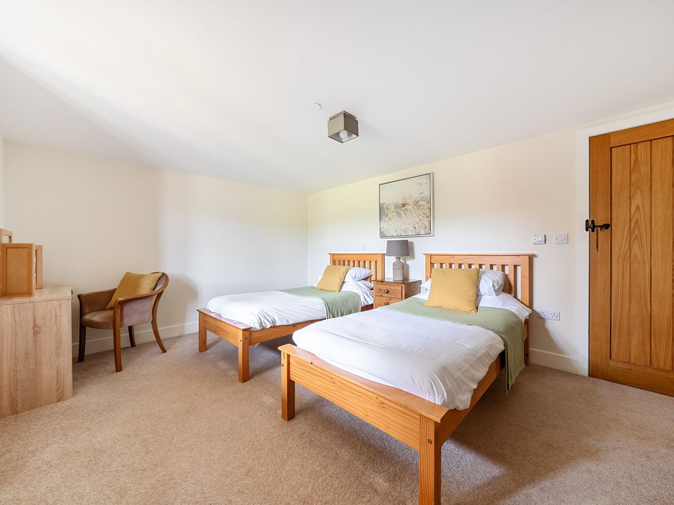 A bedroom with two single beds and a chair at The Granary in Corwen
