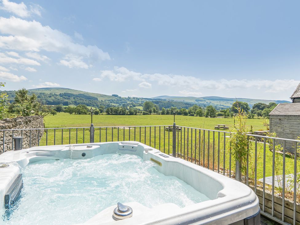A hot tub overlooking a field and mountains at The Granary in Corwen