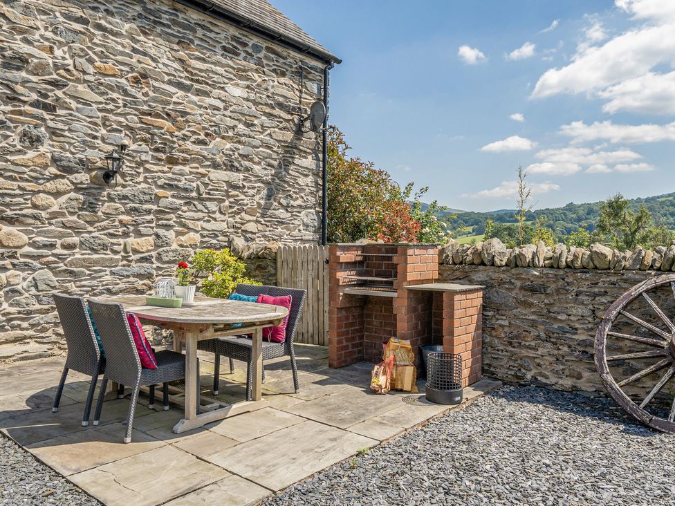 An outdoor dining area with a stone wall and grill at The Granary in Corwen
