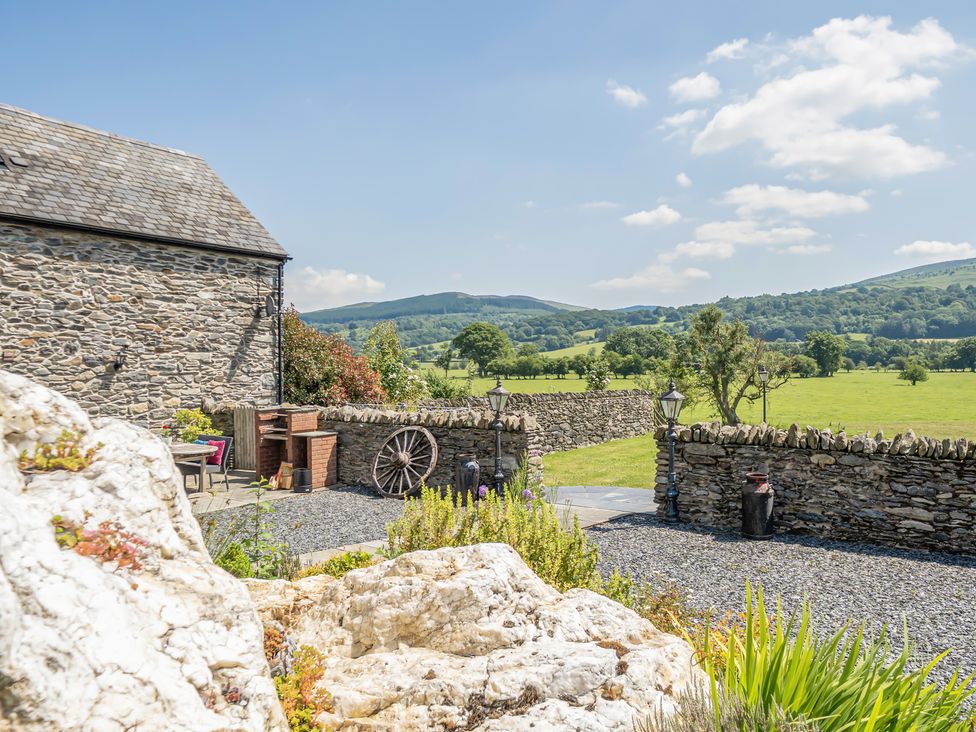 A garden with a stone barn and seating area at The Granary in Corwen