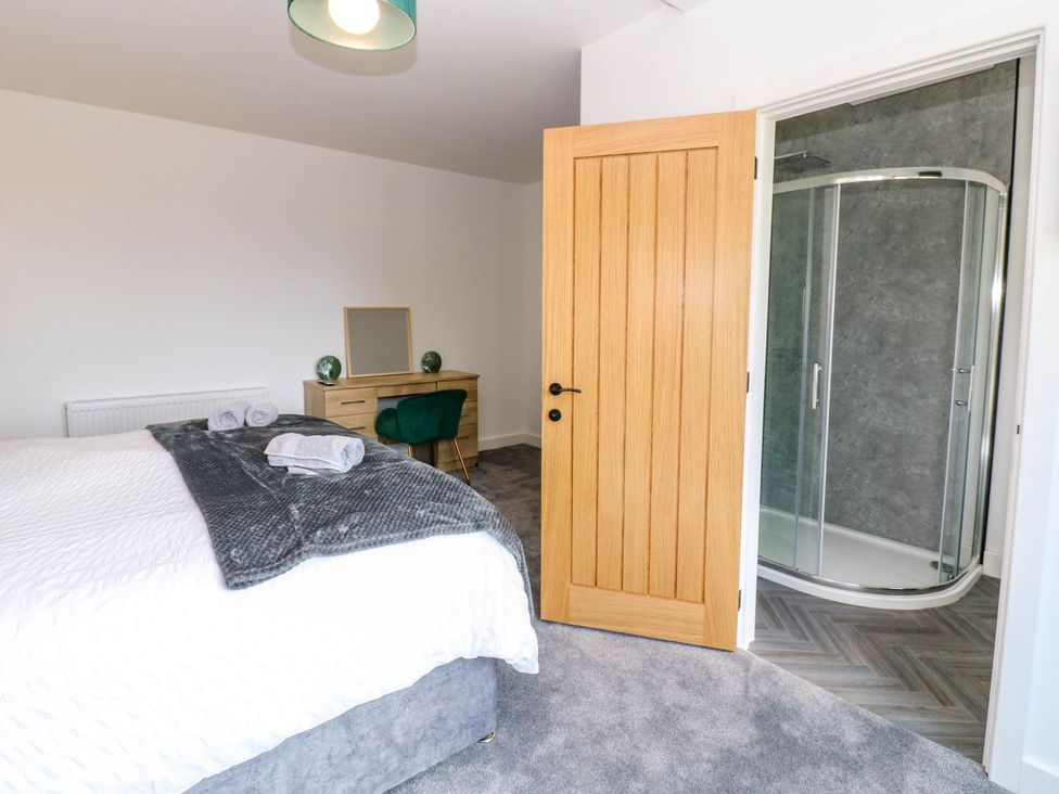 A bedroom with a bed, dresser, towels, and attached shower at Sycamore Cottage in Frizington