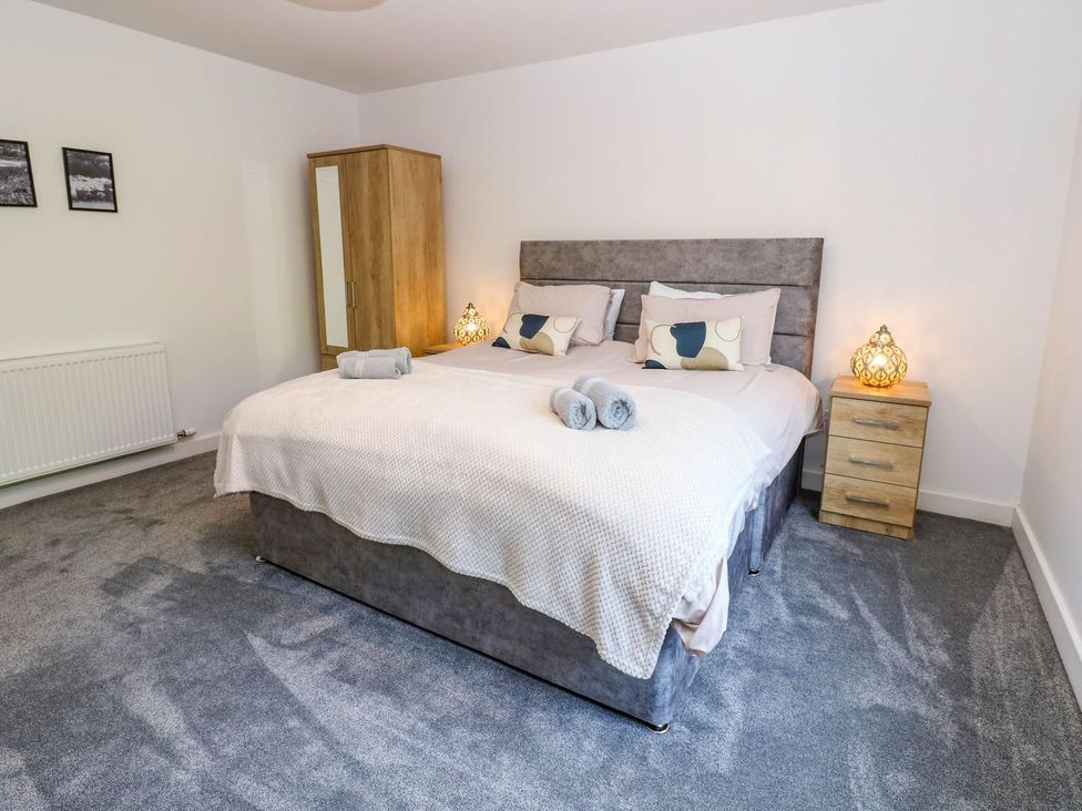 A bedroom with a bed, bedside table, wardrobe, and towels at Sycamore Cottage in Frizington