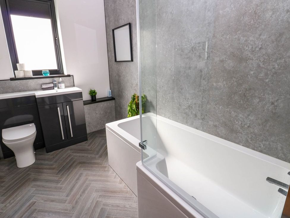 A bathroom with a bath tub, toilet, and sink at Sycamore Cottage in Frizington