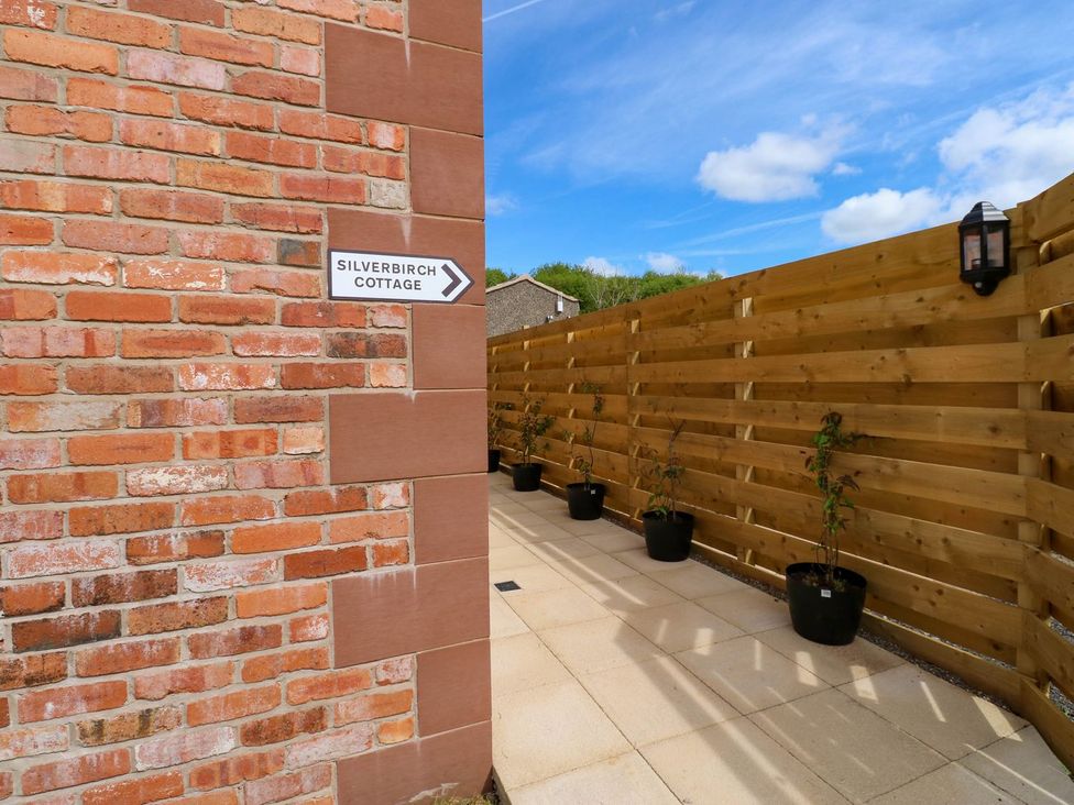 An outdoor pathway with potted plants and a sign at Silver Birch Cottage in Frizington