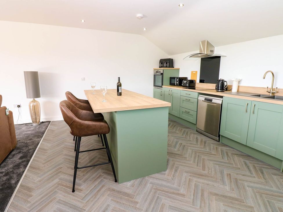 A kitchen with bar stools and appliances at Silver Birch Cottage in Frizington